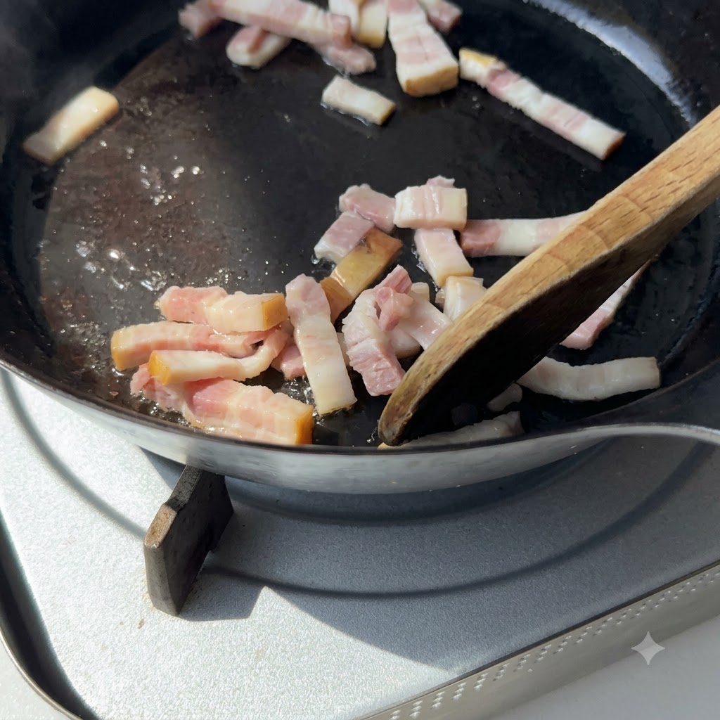 Une spatule en bois remuant des morceaux de bacon dans une poêle en fonte sur une plaque de cuisson.