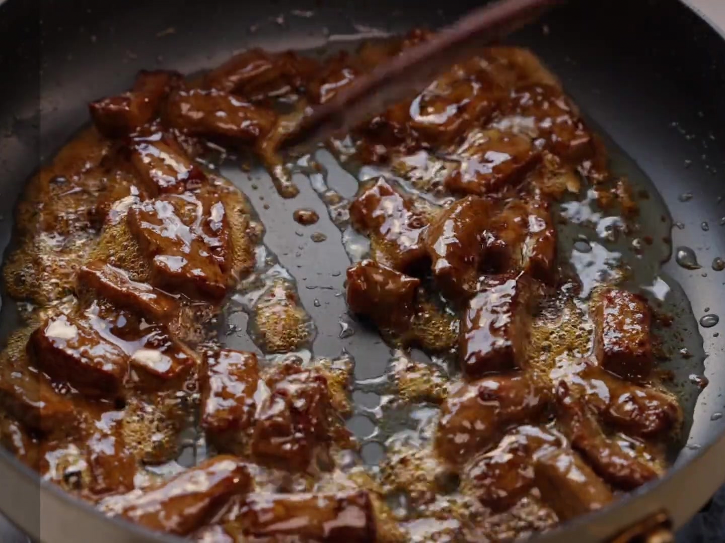 Des lamelles de poivrons et doignons incorporées à une poêle contenant des morceaux de steak bruns.