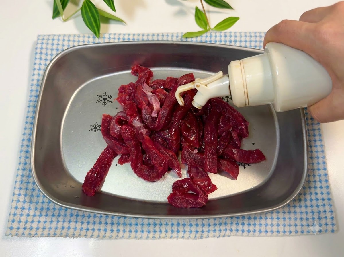 Des lanières de bœuf dans un plateau en métal assaisonnées avec de lhuile et de la sauce soja.