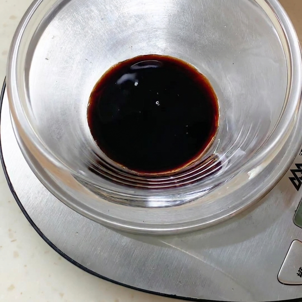 Mélange de sauce foncée à lintérieur dun bol en verre posé sur une balance de cuisine numérique.