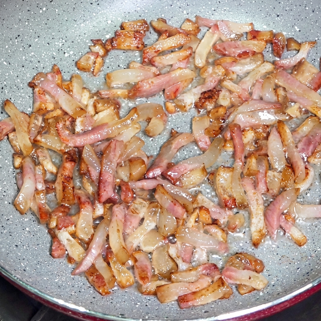 Des lanières de guanciale dorant dans une poêle, libérant leur graisse et devenant croustillantes sur les bords.