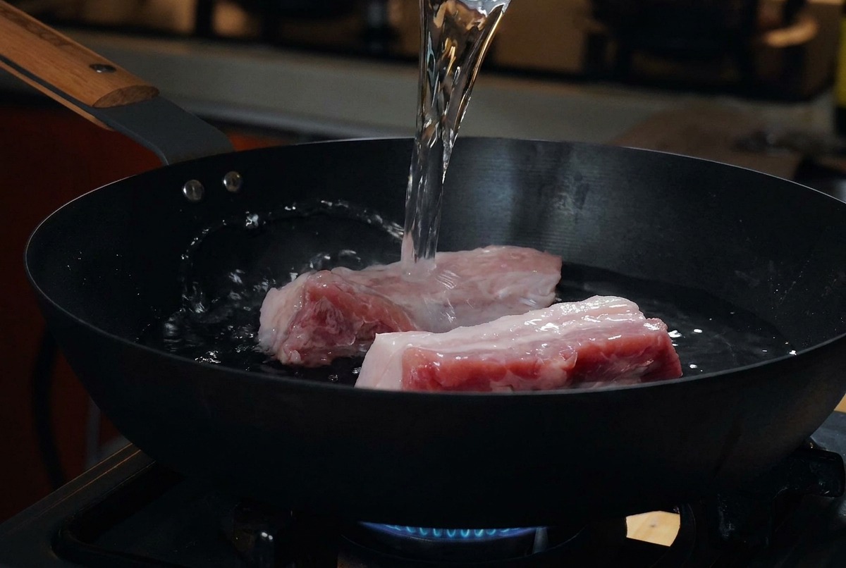 Tranches épaisses de poitrine de porc crue reposant dans une poêle froide pendant quon y verse de leau.