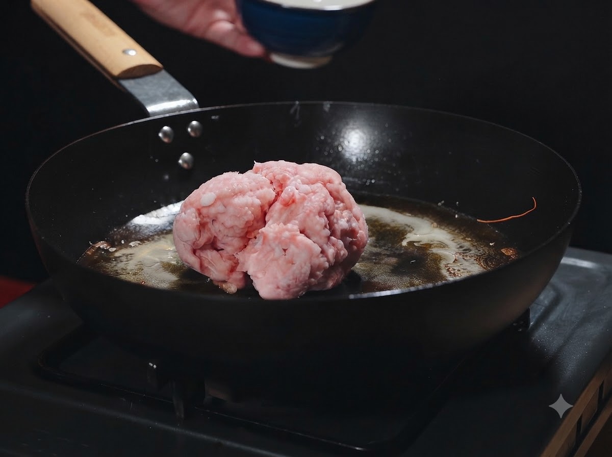 Une boule de viande hachée crue posée dans une poêle chaude avec de lhuile de crevette au moment dêtre ajoutée.