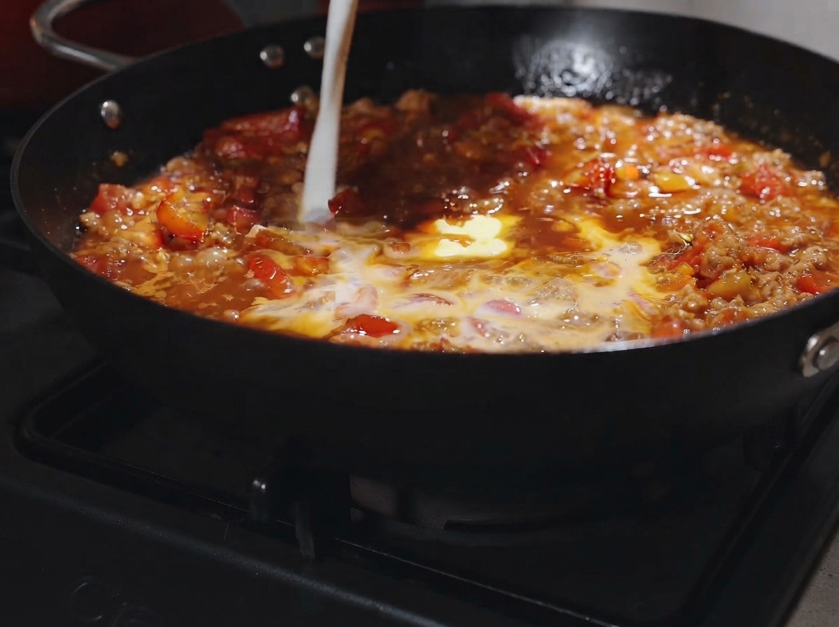 Une noix de beurre et un filet de lait versés dans la sauce tomate et viande bouillonnante.