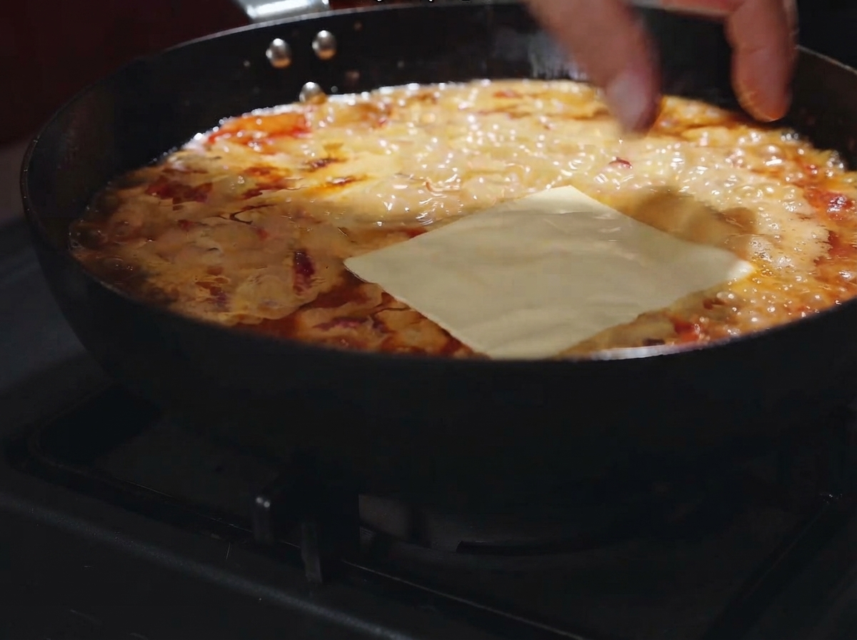 Une tranche de fromage posée à plat sur la sauce crémeuse frémissante dans la poêle.