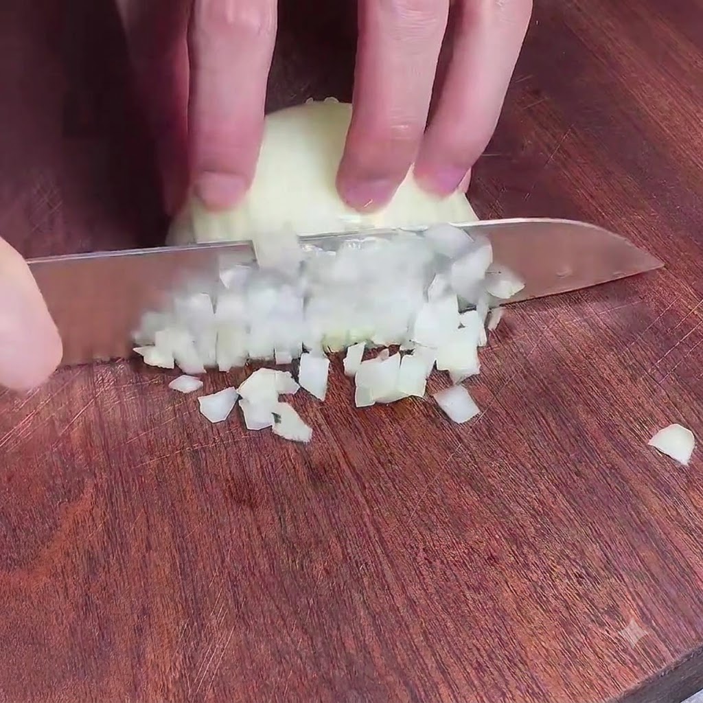 Mains découpant finement un oignon sur une planche à découper en bois avec un couteau de chef.