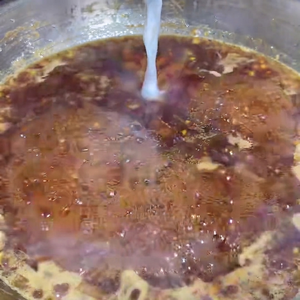 Un mince filet deau féculée coulant dans la sauce au poivre noir bouillonnante.