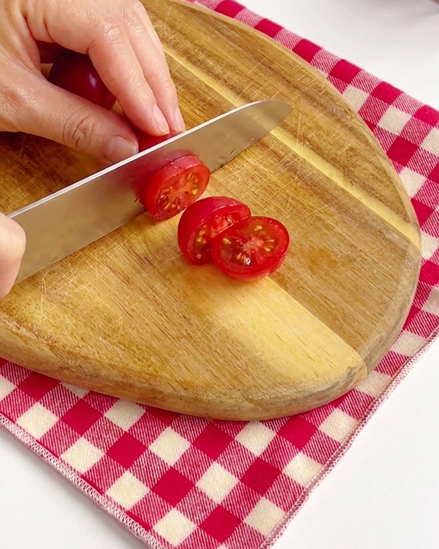 Mains tranchant des tomates cerises rouge vif en deux sur une planche à découper en bois.