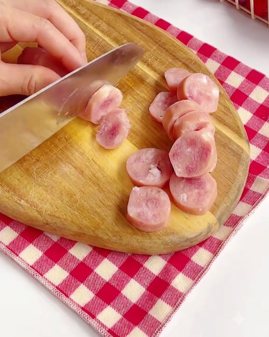 Tranchage de saucisses roses en rondelles sur une planche à découper en bois.