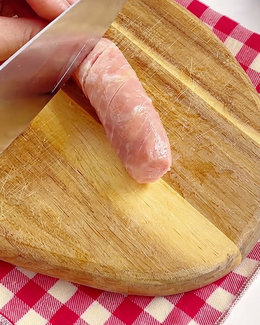 Une main incisant délicatement la surface dune saucisse entière avec un couteau sur une planche en bois.