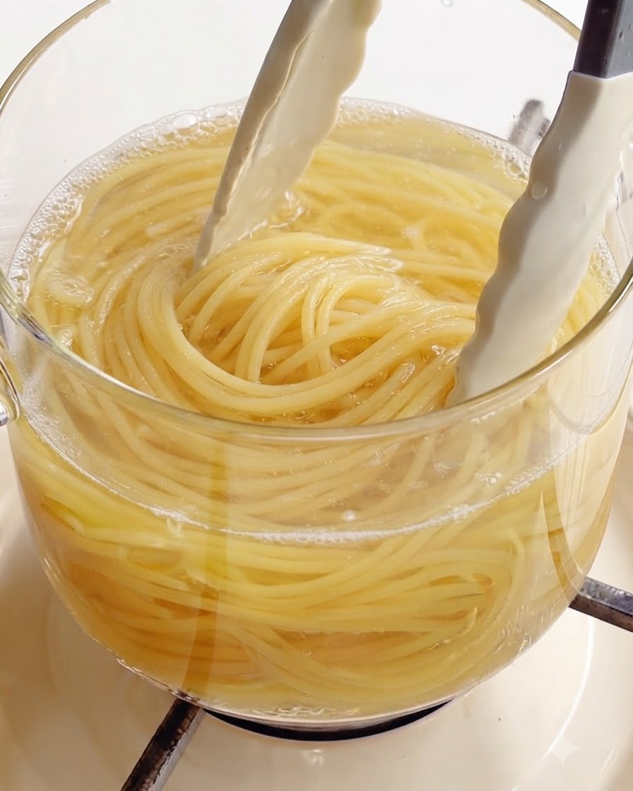 Utilisation de pinces de cuisine blanches pour sortir des spaghettis parfaitement cuits dune casserole deau bouillante en verre.