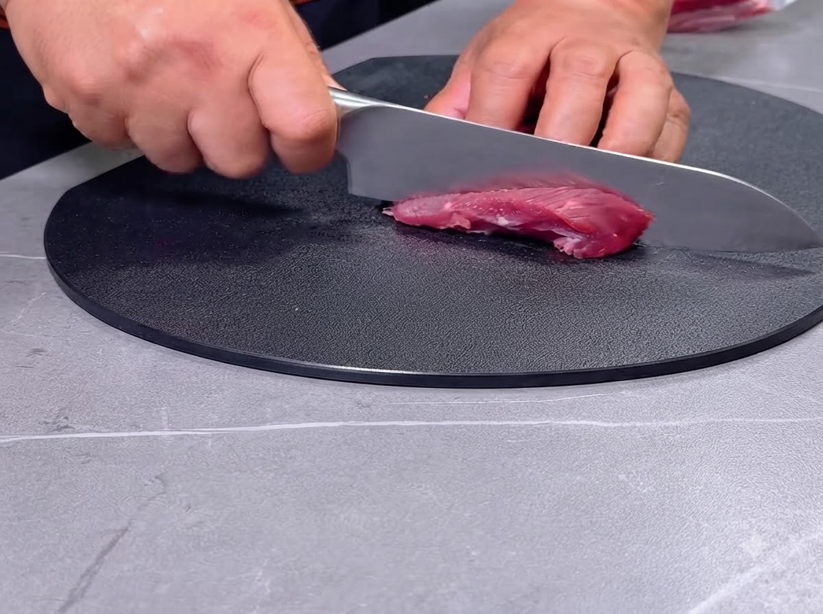 Une personne coupant de la viande de bœuf cru en morceaux avec un couteau sur une planche à découper noire.