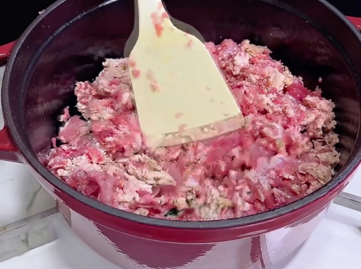 Utilisation dune spatule blanche pour faire sauter de la viande hachée dans une cocotte en fonte rouge alors quelle commence à dorer.