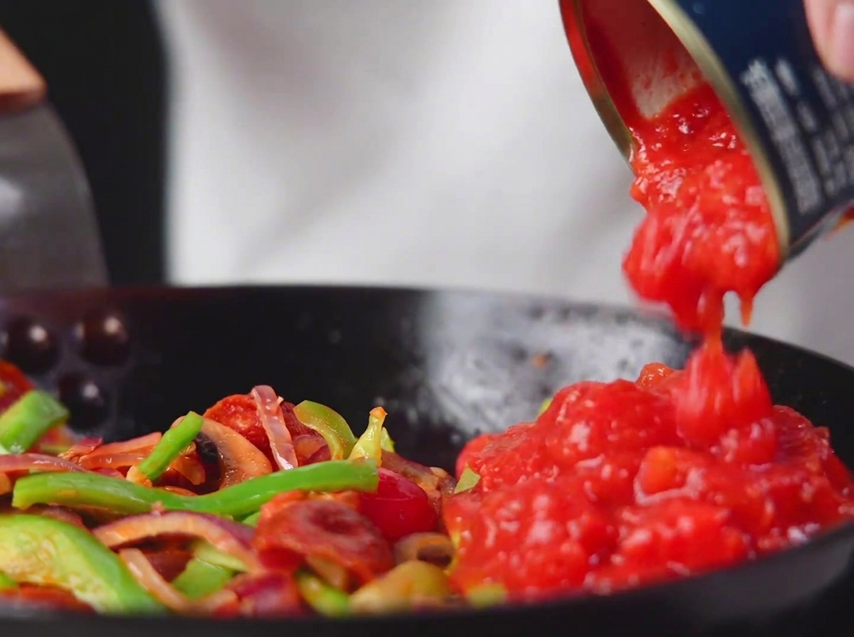 Tomates concassées en conserve versées dans la poêle avec les légumes et le salami.