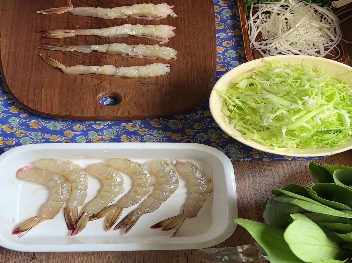 Plusieurs crevettes crues décortiquées alignées sur une planche à découper en bois après avoir préparé les tendons du ventre.