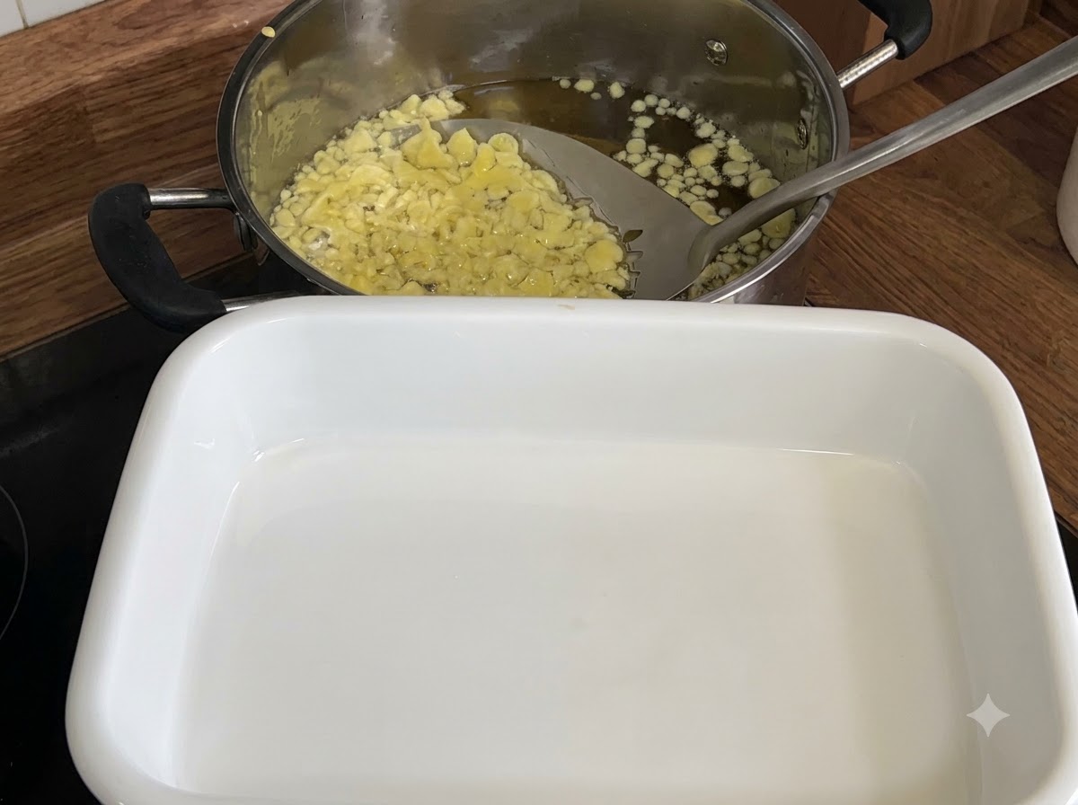 Une cuillère écumoire ramassant des flocons de tempura frits jaune pâle dune casserole dhuile vers un plateau blanc.