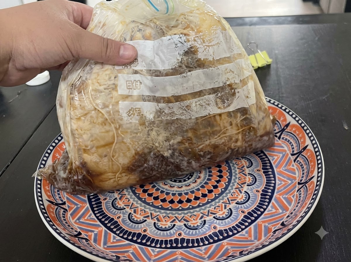 Une main tenant un sachet de viande mariné sous vide posé sur une assiette à motifs.