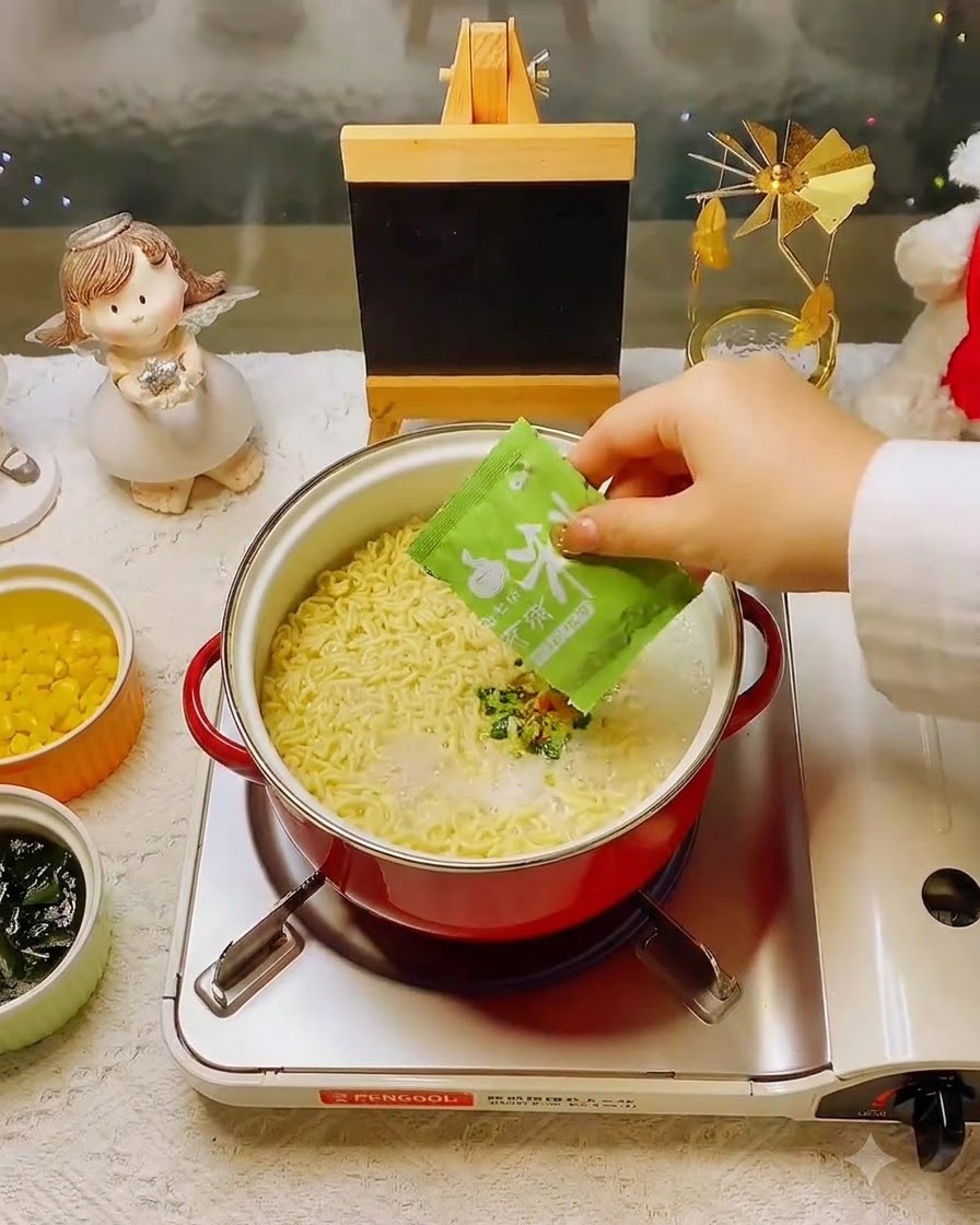 Une main ajoutant un sachet dassaisonnement vert dans la casserole de nouilles et de bouillon.