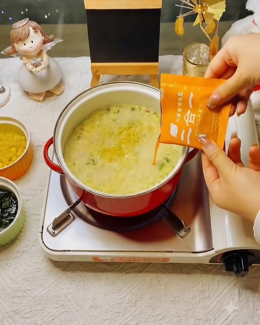 Un sachet de soupe dassaisonnement orange versé dans la casserole de nouilles frémissantes.