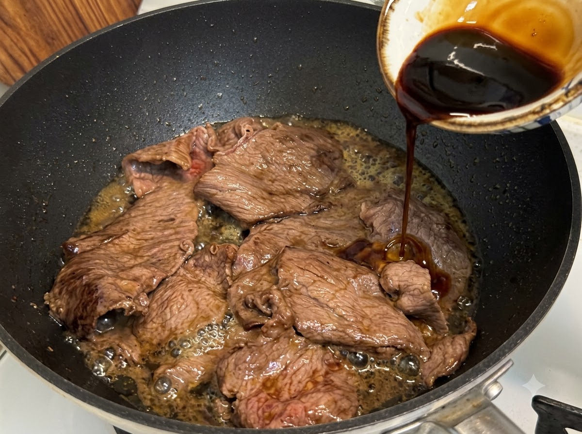 Sauce teriyaki versée dans une poêle sur des tranches de bœuf pour mijoter et réduire.
