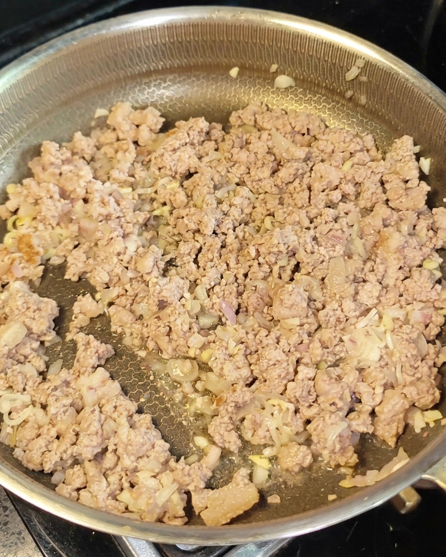 Viande hachée dorée et aromates étalés dans une poêle avec de la pâte de miso rouge en cours dincorporation.