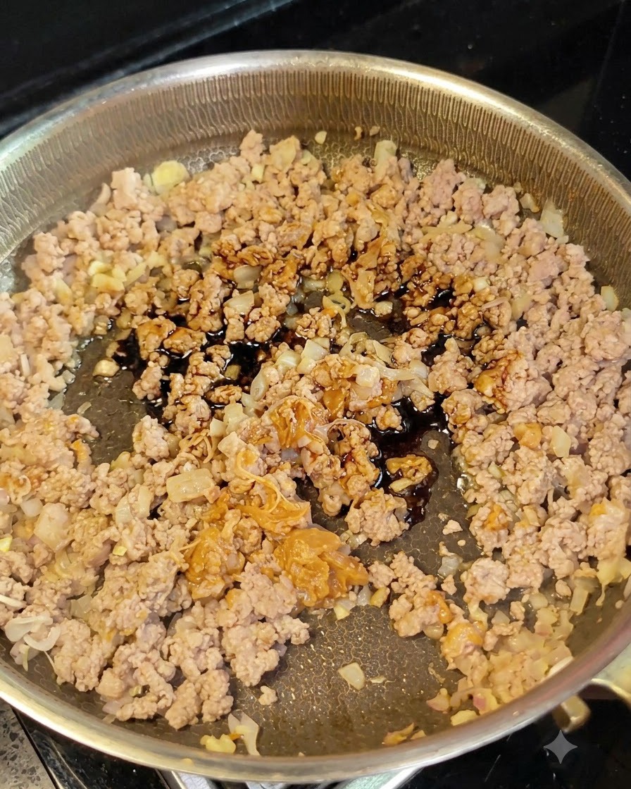 De la sauce soja noire versée dune petite cuillère sur la viande hachée et les oignons dans une poêle.