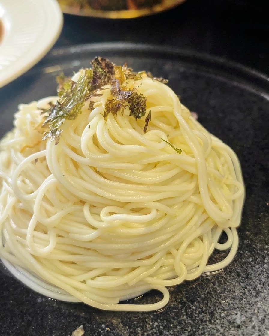 Flocons dalgues séchées écrasées saupoudrés sur une spirale de nouilles ramen cuites disposées sur une assiette sombre.