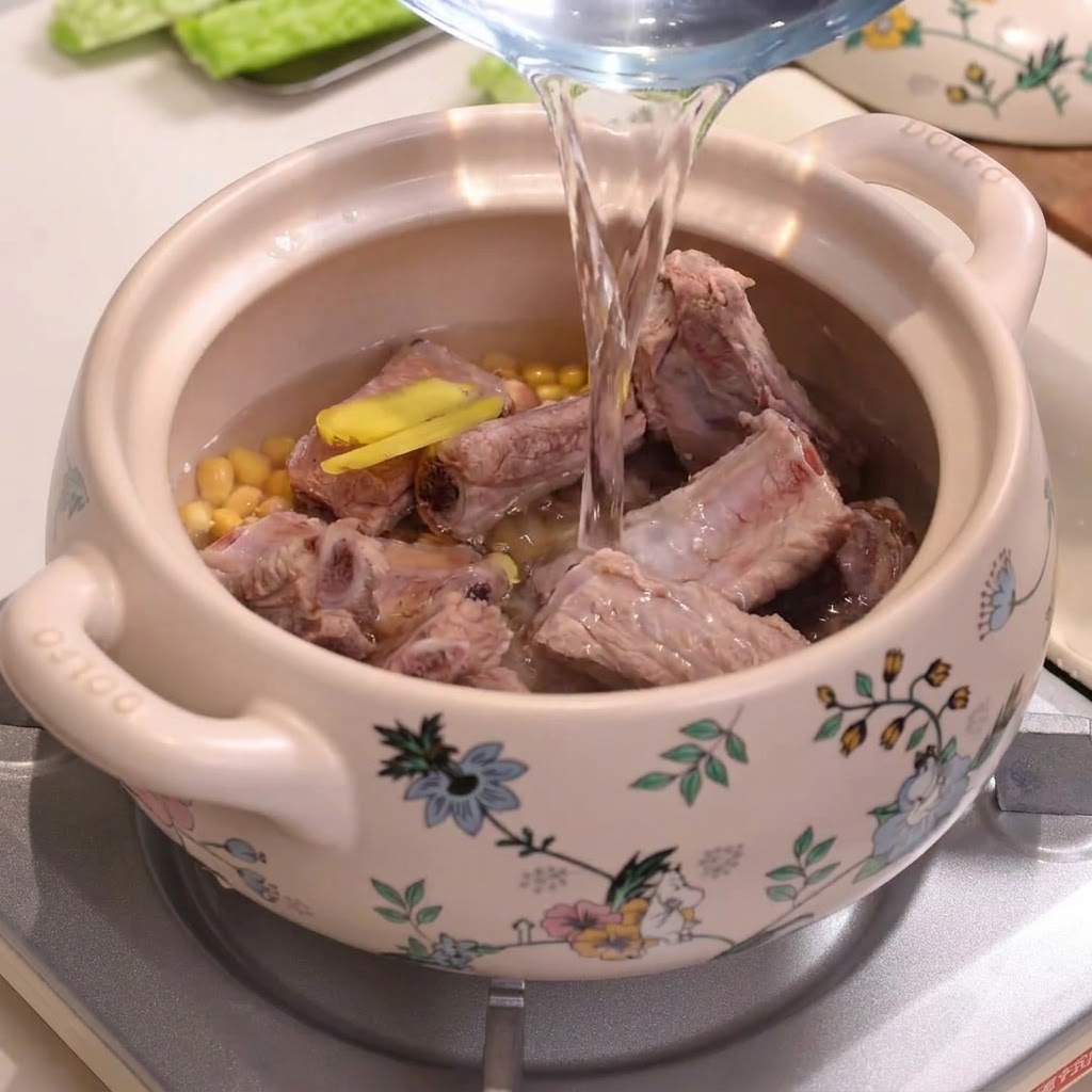 De leau est versée dun pichet dans une marmite en céramique décorée remplie de travers de porc et de graines de soja.