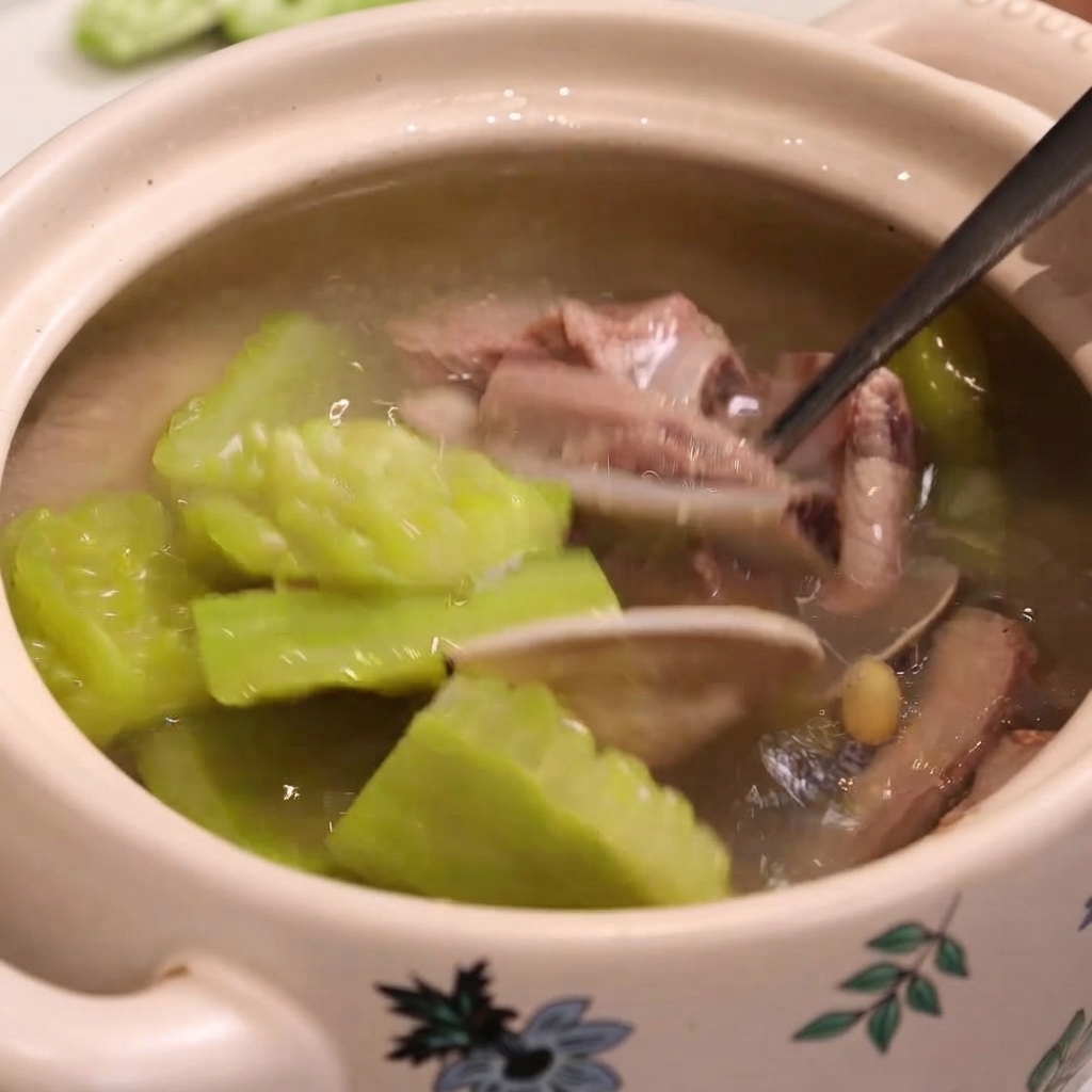 Une cuillère en métal prélève une palourde, un morceau de travers de porc cuit et de la margose dune marmite de soupe.