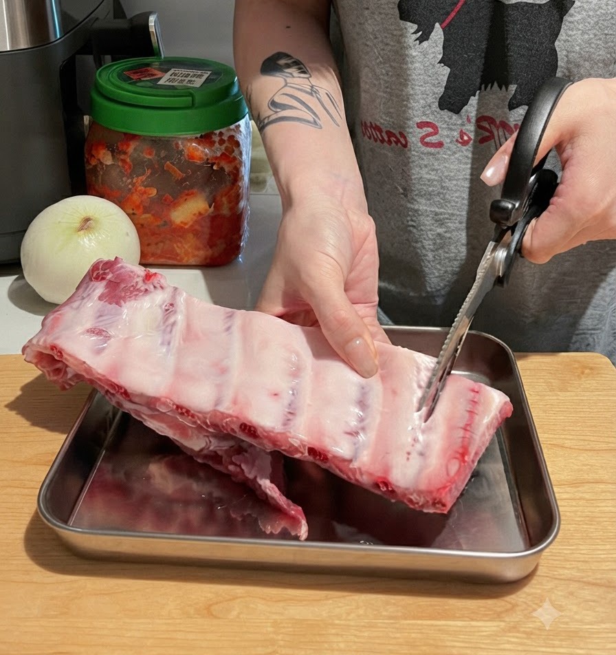 Mains découpant un grand carré de travers de porc cru en morceaux individuels sur une planche avec des ciseaux.