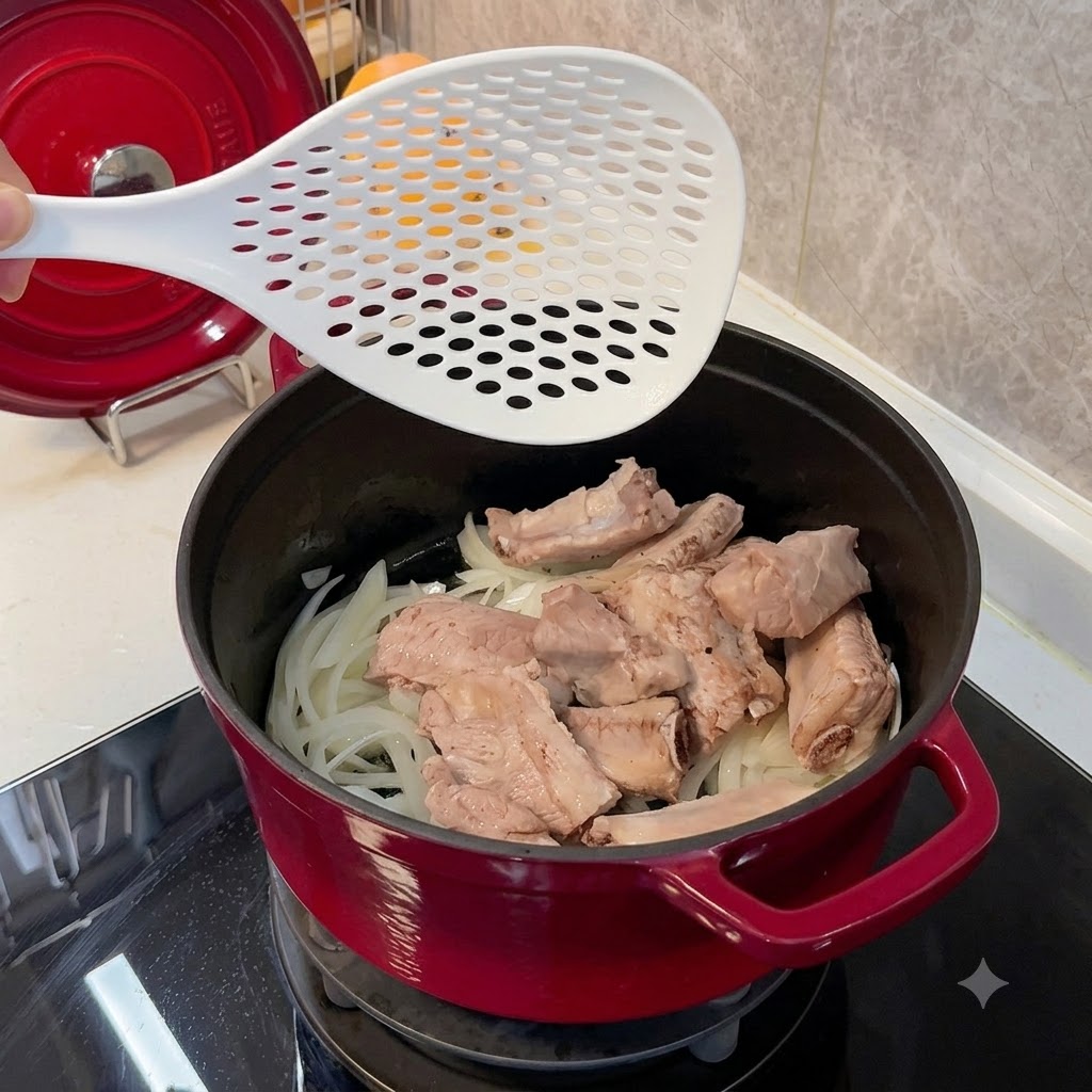 Dépôt des travers de porc blanchis dans une cocotte rouge sur un lit doignons ramollis.