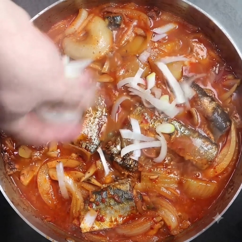 Des oignons verts blancs hachés saupoudrés sur une casserole de poisson braisé frémissant.