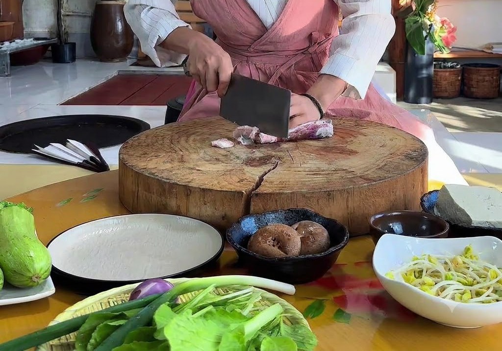 Mains utilisant un hachoir pour trancher de la poitrine de porc crue sur une grande planche à découper ronde en bois.