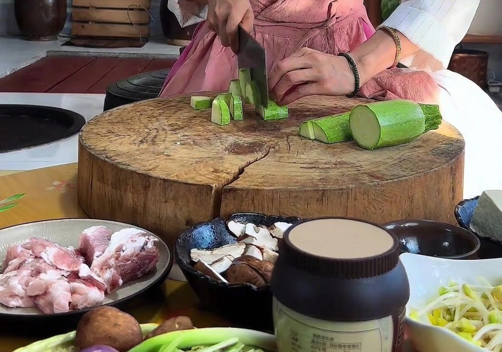 Mains coupant une courgette verte en morceaux triangulaires avec un hachoir sur une planche à découper ronde en bois.