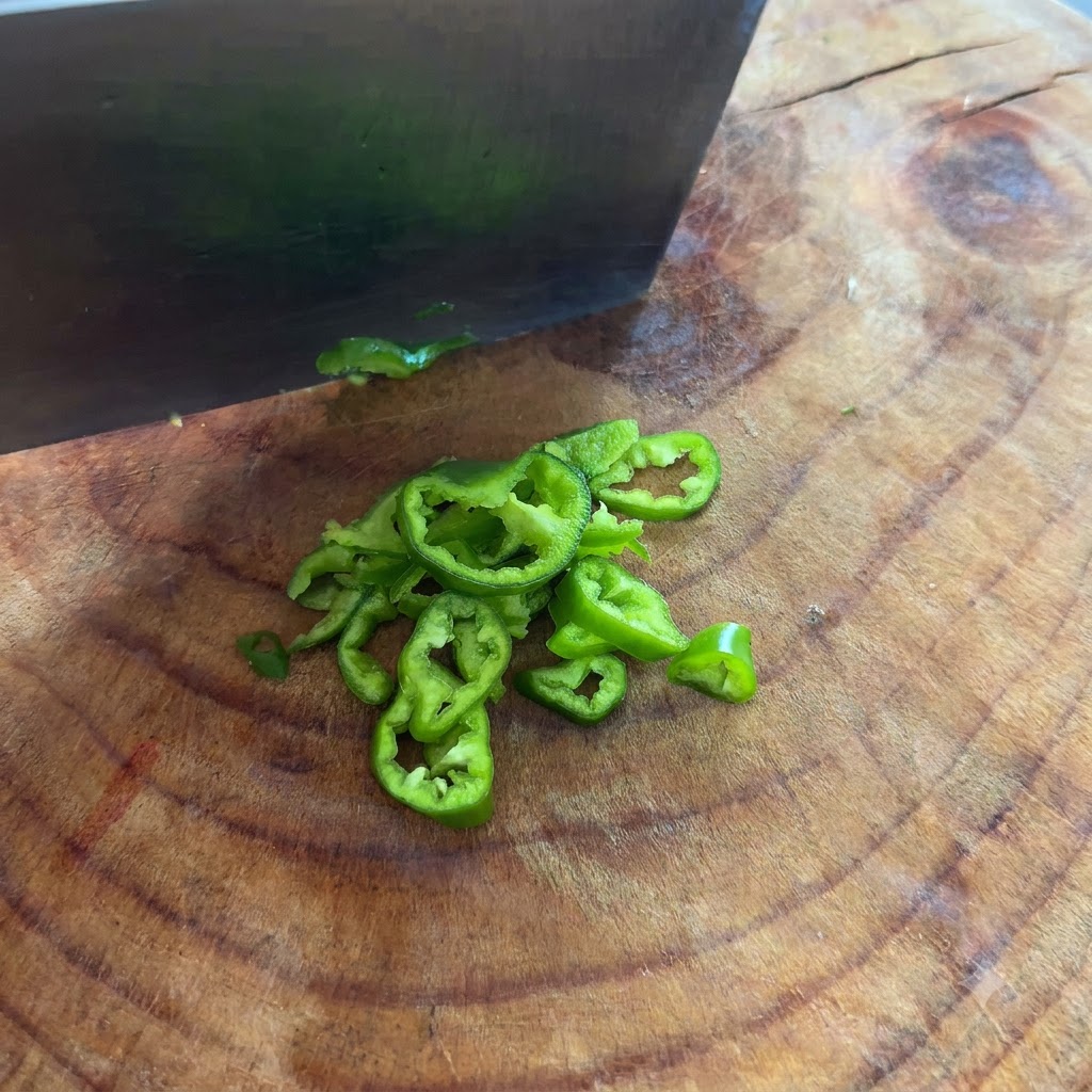 Des piments verts coupés en fines rondelles avec un couteau sur une planche à découper.
