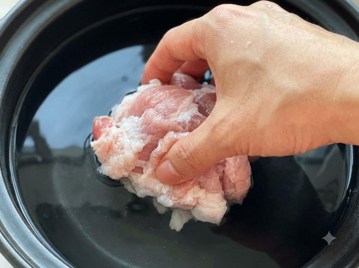 Des morceaux de porc crus en train dêtre immergés dans une casserole remplie deau froide et de pâte de soja.