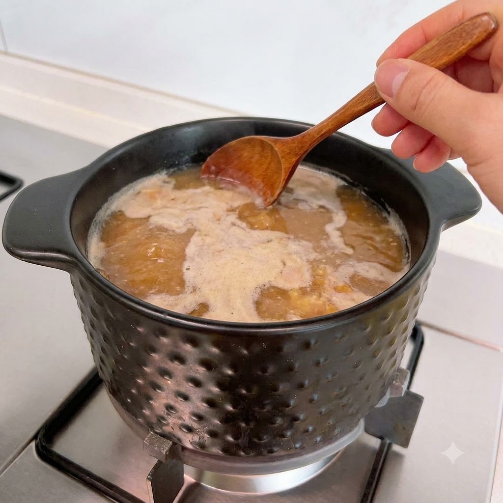 Une cuillère en bois retirant lécume à la surface de la soupe frémissante.