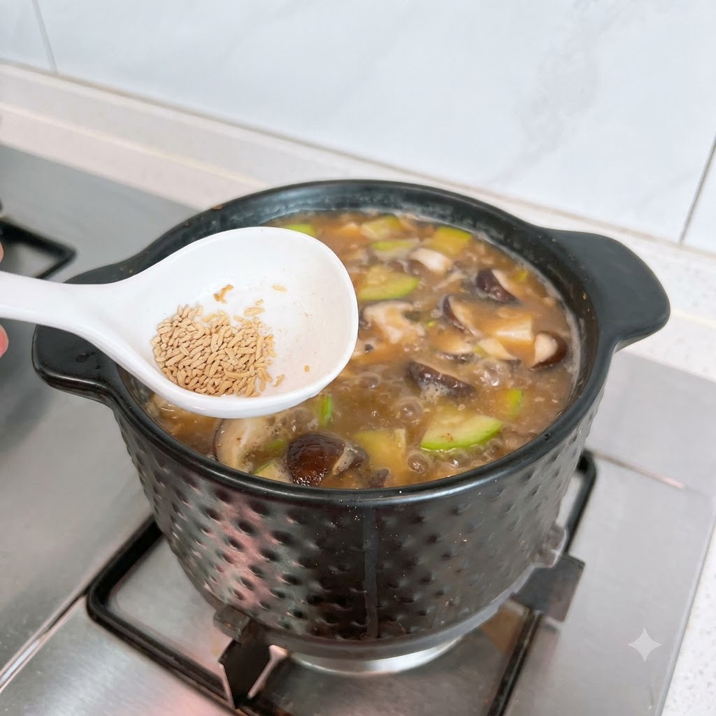 Une cuillère blanche contenant du bouillon de bœuf en poudre au-dessus de la casserole de Doenjang Jjigae.