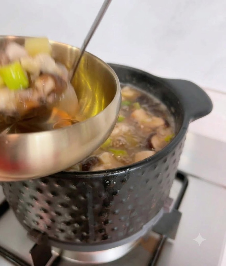 Une louche servant la soupe à la pâte de soja fumante depuis une casserole noire vers un bol de service en métal.