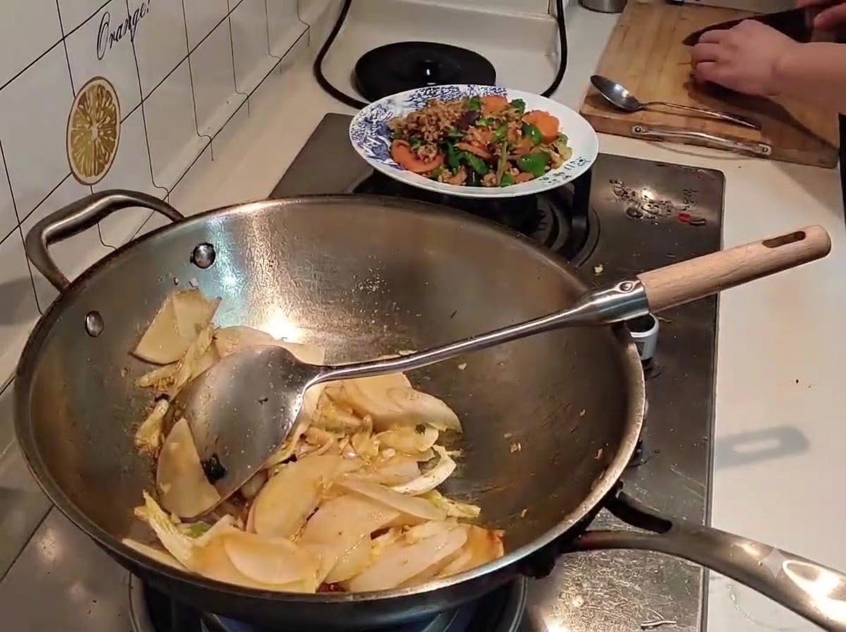De leau versée dune bouilloire noire dans un wok rempli de radis et de chou émincés.