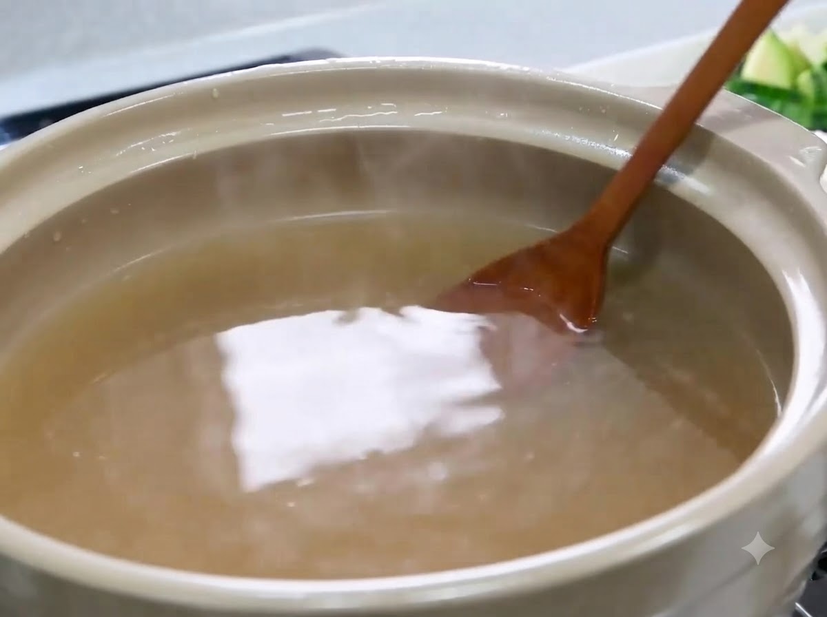 Une cuillère en bois mélangeant et dissolvant la pâte de soja dans un bouillon marron clair.