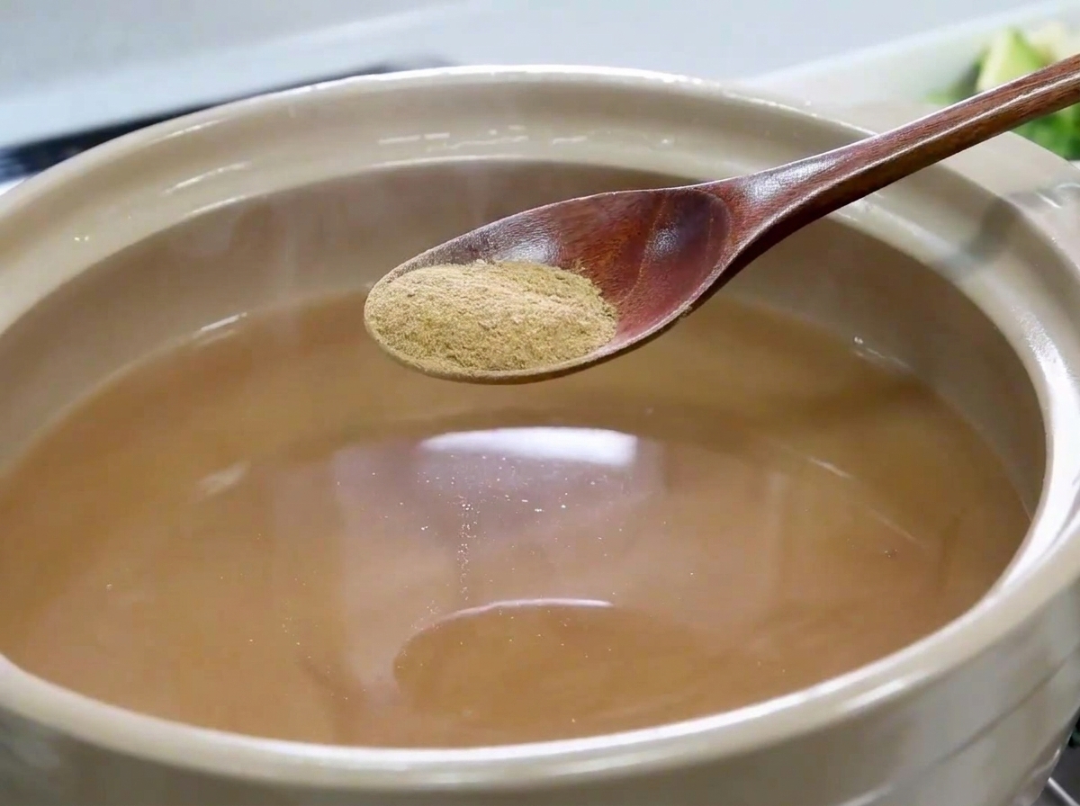 Une cuillère en bois saupoudrant de la poudre danchois au-dessus du bouillon.