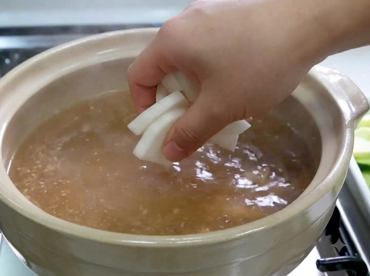 Une main déposant des tranches de radis blanc dans le bouillon frémissant.