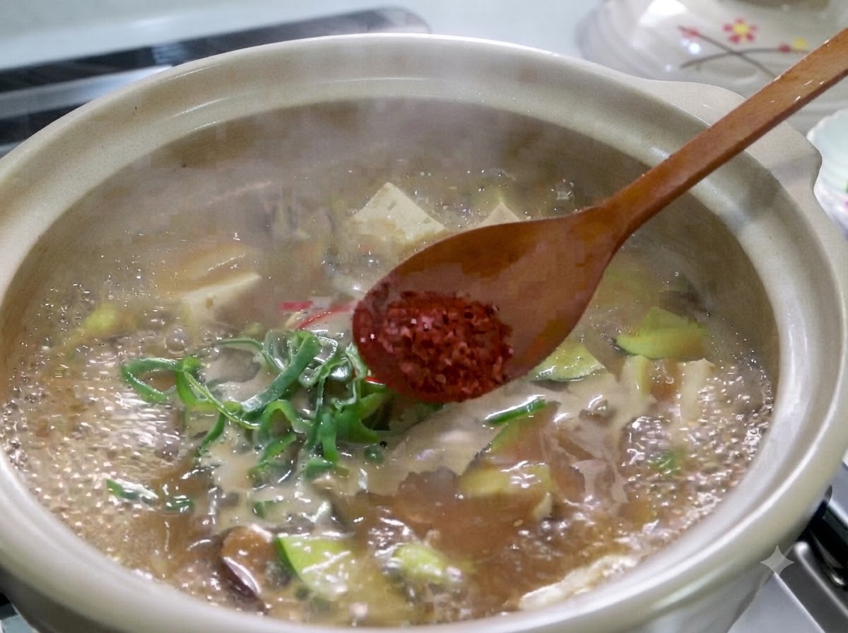 Une cuillère en bois saupoudrant de la poudre de piment rouge sur un ragoût de pâte de soja coréen bouillant.