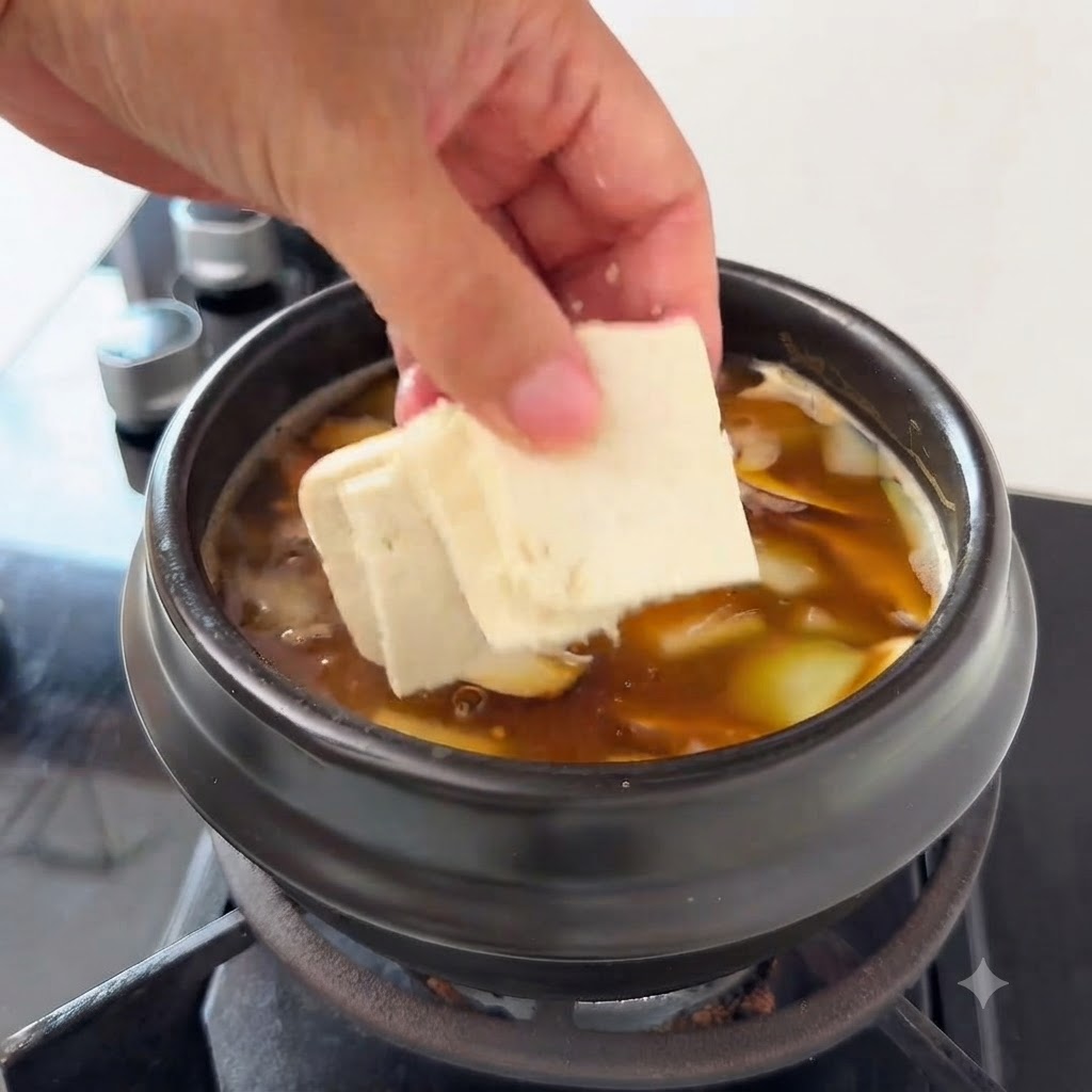 Morceaux de tofu ajoutés à la soupe contenant des tranches de courgette et des champignons enoki.