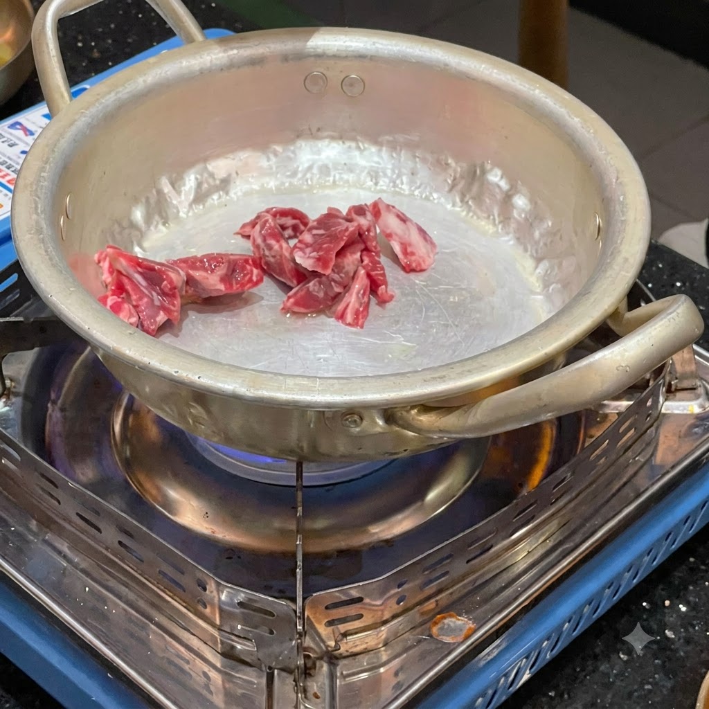 Des morceaux de bœuf cru en train dêtre sautés dans une petite casserole en métal sur un réchaud à gaz portable allumé.