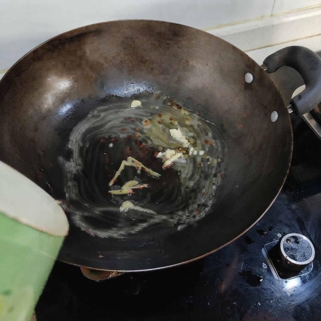De leau bouillante versée dun récipient vert dans un wok contenant du saindoux fondu, du gingembre et de lail.