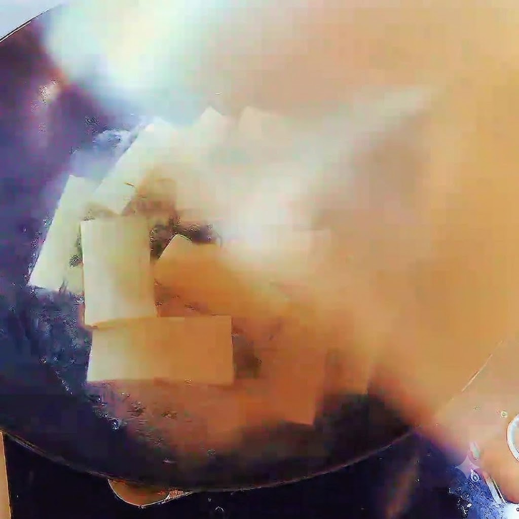 Un wok rempli de soupe bouillante et de lanières de tofu, couvert hermétiquement par un couvercle.