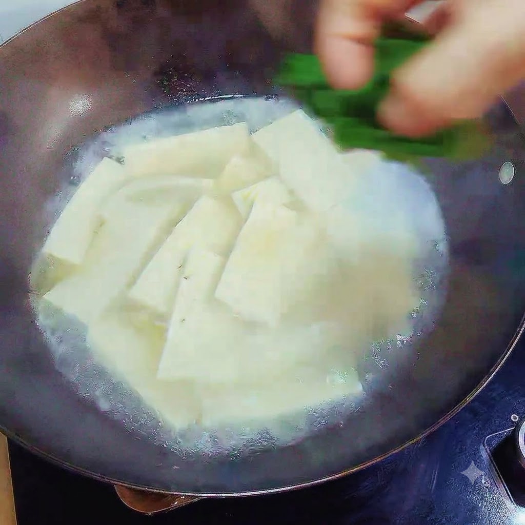 Une main laissant tomber des oignons verts hachés sur la soupe au tofu finie dans le wok.