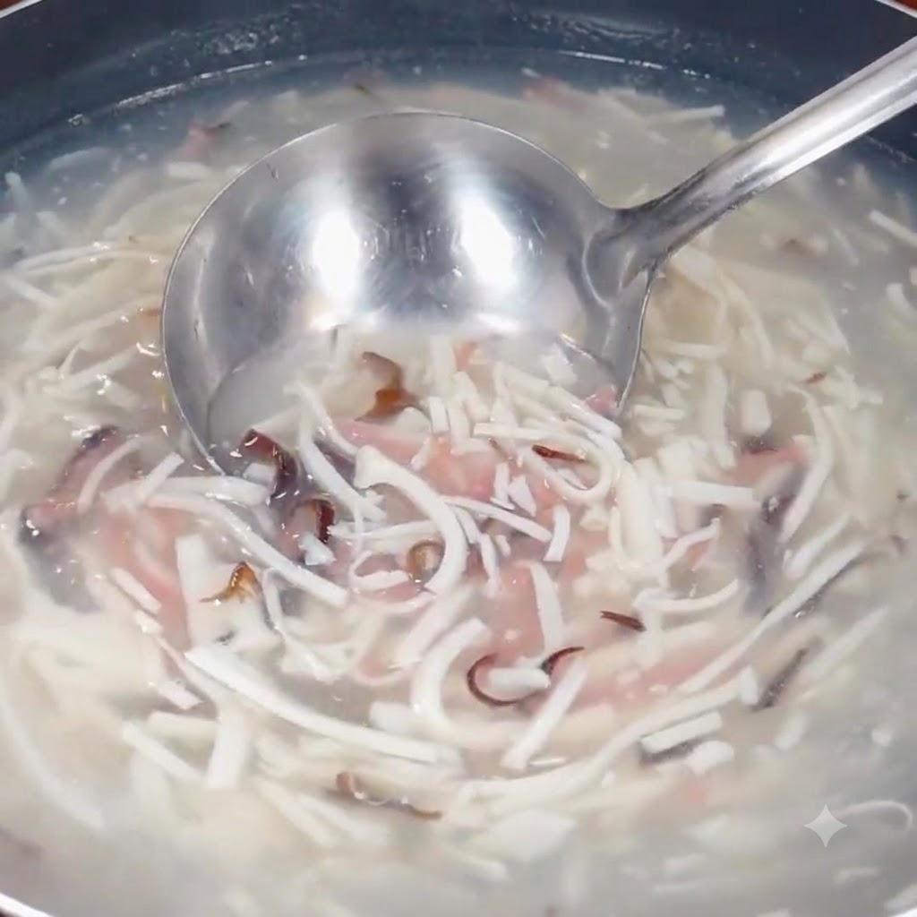 Une louche puisant dans le mélange de soupe frémissante contenant des ingrédients émincés dans une casserole.